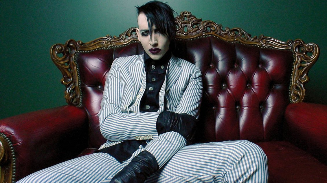 Download Wallpaper Marilyn Manson in a suit with stripes on the red sofa