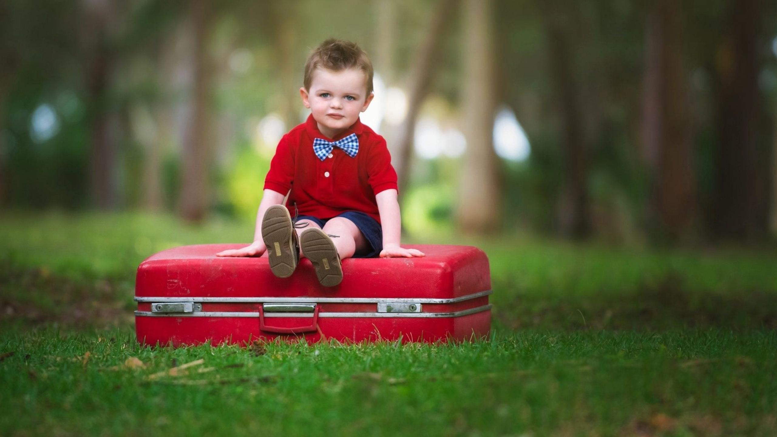 Cute baby boy with bow on a red suitcase