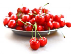 A bunch of three cherries and a plate full of cherries