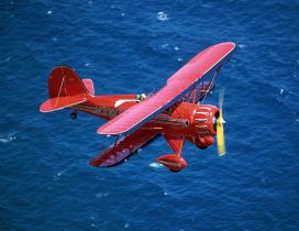 Red airplane flying above the blue sea