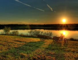 A motorcycle with trailer near the river in the sunset