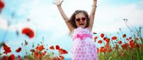 Happy baby girl in white and pink dress on the poppies field