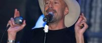 Bruce Willis at the microphone with a hat on the head
