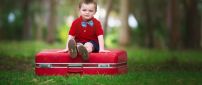 Cute baby boy with bow on a red suitcase