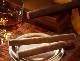 A glass with whiskey and cigars on a table
