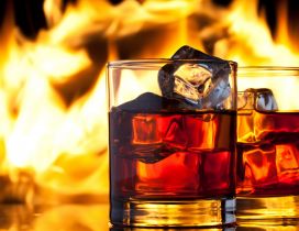 Two glasses of whiskey with ice - fire on background